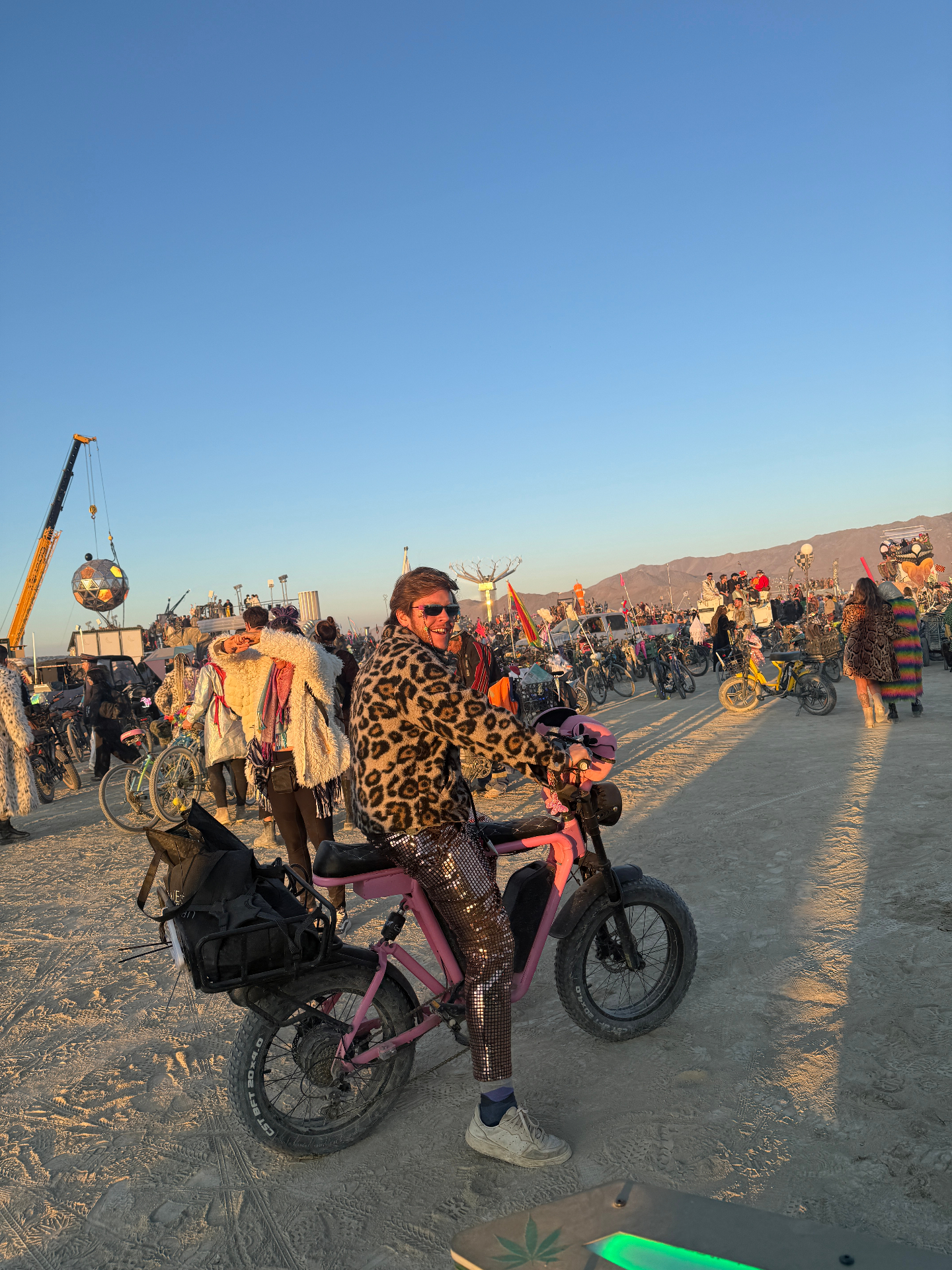 Rider in leopard fur coat and disco pants on a pink DUST eBike among a crowd on the playa