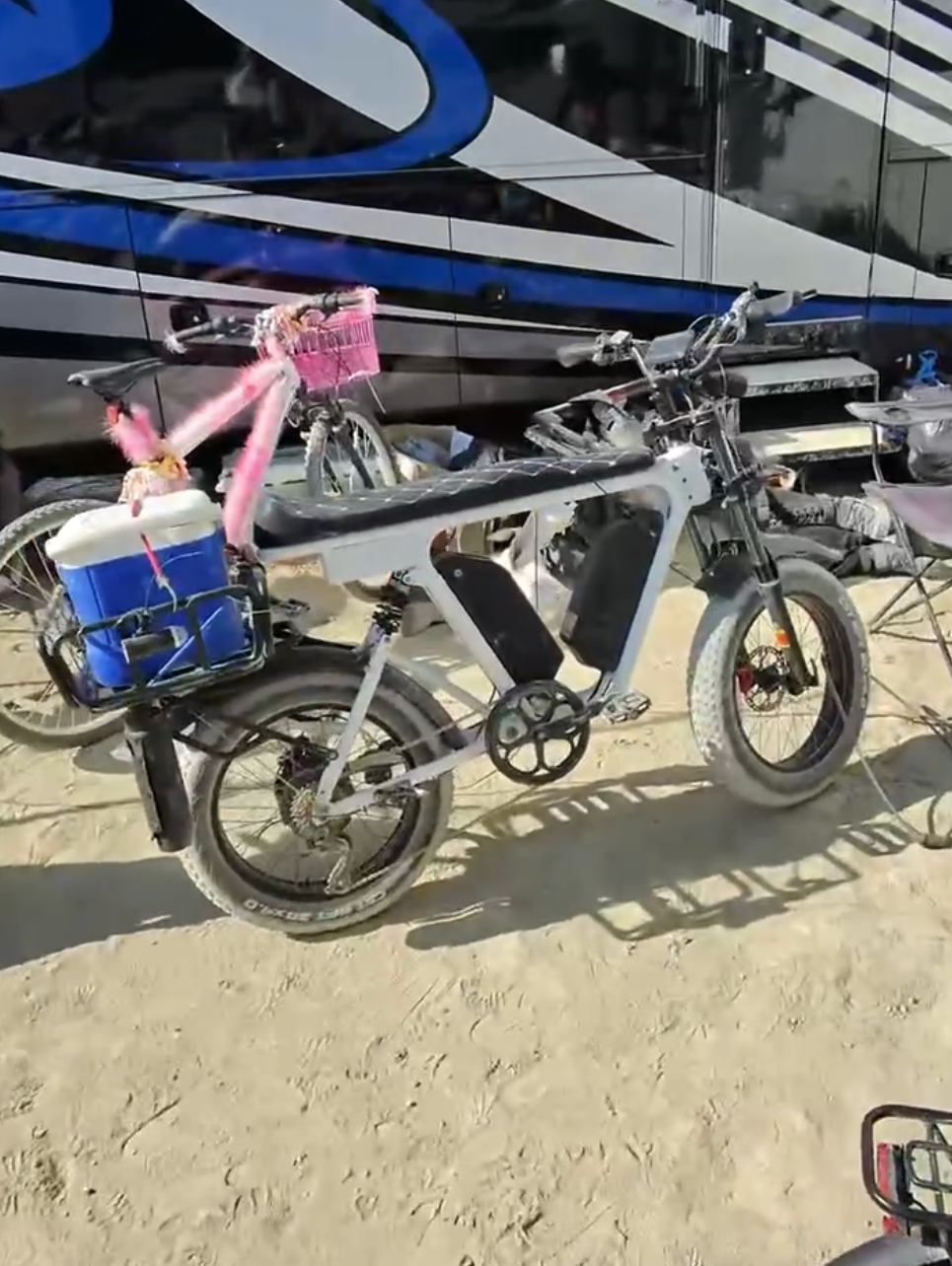White DUST eBike loaded with a cooler and pink fur, parked in the sand